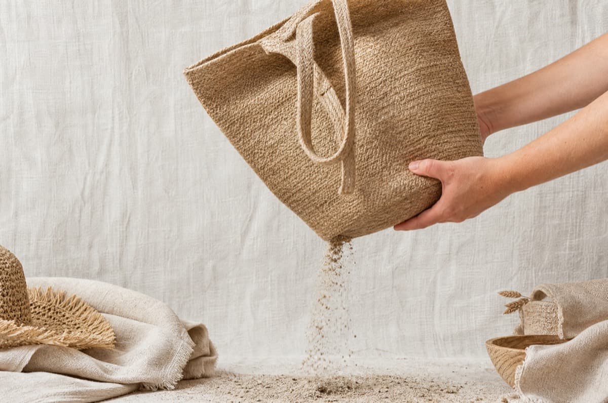 Hands shaking sand out of a jute beach bag