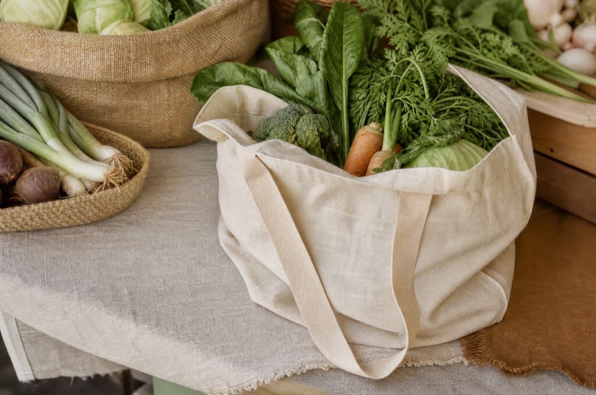 An open canvas tote loaded with vegetables at a market stall